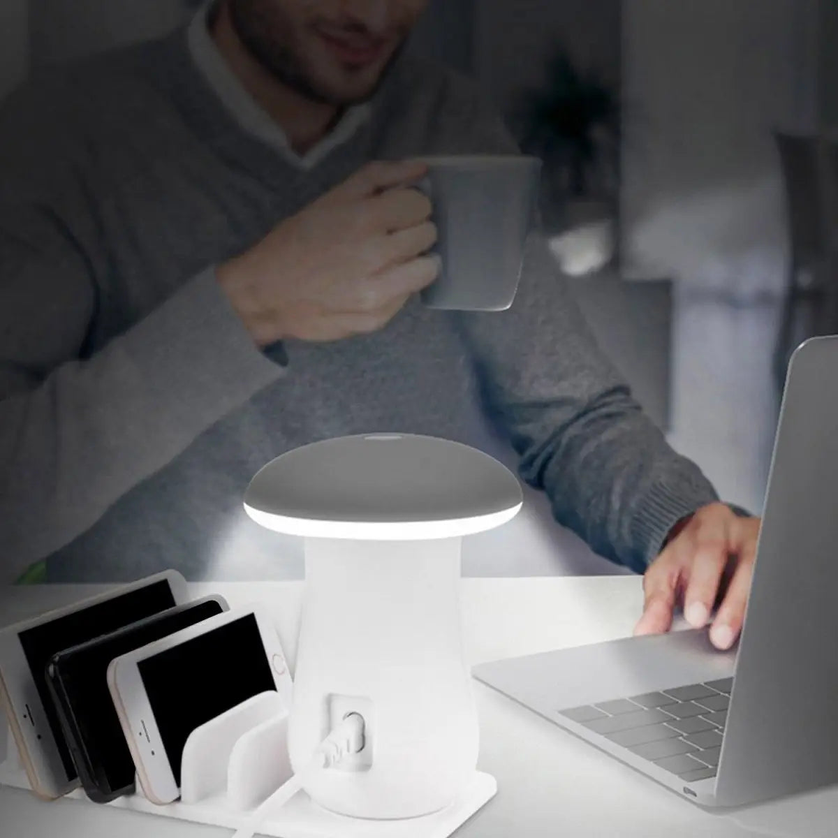 Person using a desk setup with a lamp, laptop, and phone on a table.