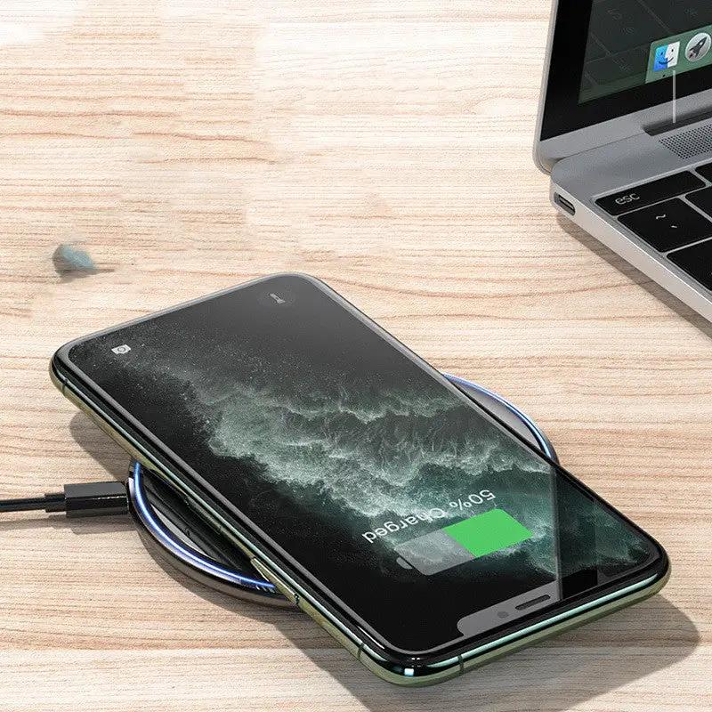 Smartphone with wireless charging pad on a wooden surface next to a laptop.