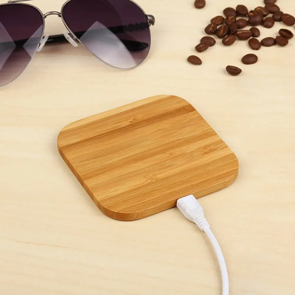 Wooden charging pad with a cable on a beige surface with sunglasses and coffee beans.